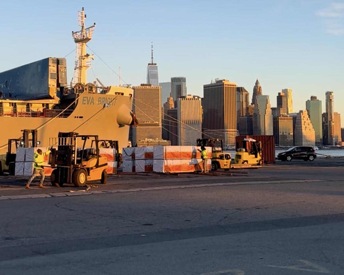 Forklifts working a vessel discharge at golden hour, Lower Manhattan behind